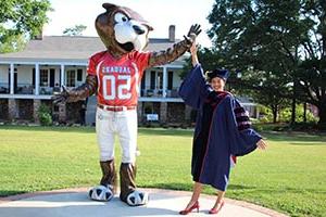 Business student in cap and gown high fiving 南paw statue on campus.